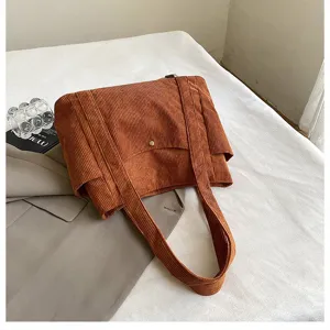 Dettaglio ravvicinato di una grande borsa tote in velluto a coste marrone su sfondo bianco