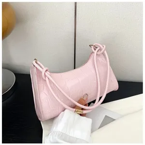 Detailed view of a hand holding a stylish pink crocodile pattern underarm bag with knot straps