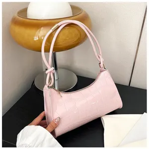Elegant pink crocodile embossed underarm handbag for women displayed on a desk with a lamp