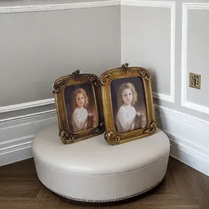 Detailed close-up of two ornate vintage gold resin photo frames on an elegant beige ottoman