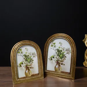 Vintage arched gold photo frame with elegant floral art on wooden table