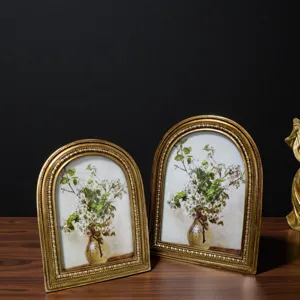 Two vintage gold arched picture frames featuring floral art displayed on a wooden surface