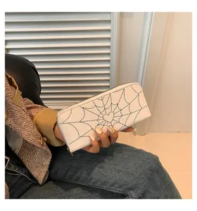 Hand holding a white long zipper wallet with stylish black spider web and heart print