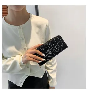 Black long wallet with white spiderweb and heart print, held by a model in a white cardigan