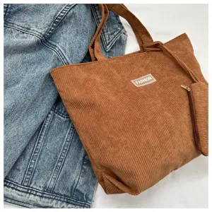 Detalle de un bolso tote de pana marrón con etiqueta FASHION y estuche a juego