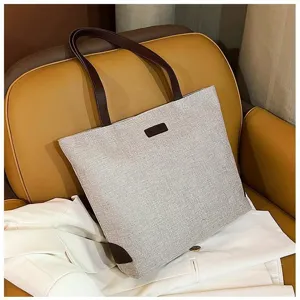 Bolso tote de lona minimalista de gran capacidad con asas y detalles de cuero marrón.