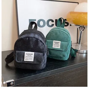 Detail view of black and green corduroy mini backpacks with front pocket labels.