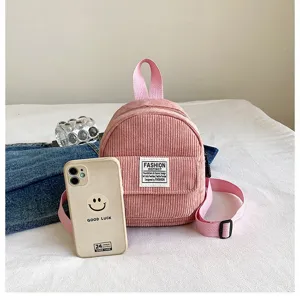 Detailed view of small pink corduroy backpack next to a phone for size comparison