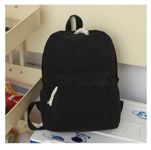 Vista detallada de mochila negra de pana con tiradores de cuerda blanca sobre caja