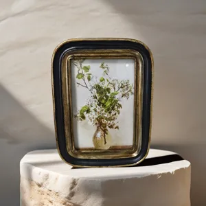 Detalle de marco de fotos vintage en resina negra y dorada con arte floral en piedra