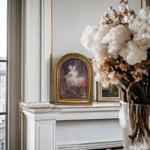 Dettaglio di un'elegante cornice dorata con dipinto classico su caminetto bianco