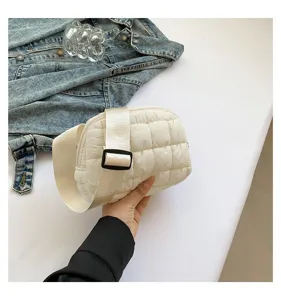 Mano sosteniendo un bolso bandolera acolchado blanco sobre fondo de chaqueta vaquera