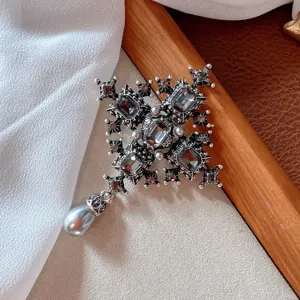 Close-up detail of vintage silver cross brooch with black rhinestones and grey pearl.