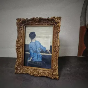 Detailed view of an ornate gold vintage photo frame displaying a classical piano painting.