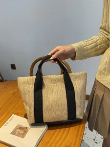 Primer plano de un elegante bolso tote de paja tejida con asas negras sobre una mesa