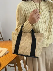 Primer plano de un bolso de paja trenzada con asas de tela negra en un ambiente acogedor.