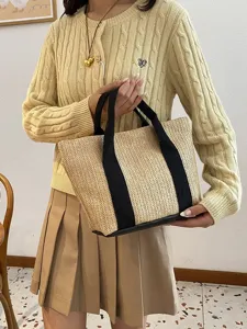 Modelo sosteniendo un elegante bolso de paja con asas negras en un ambiente acogedor.