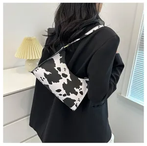 Stylish black and white cow print underarm bag for women worn with a chic black blazer.