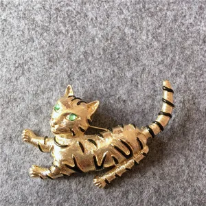 Détail d'une broche chat vintage dorée avec des yeux verts et des rayures noires élégantes.