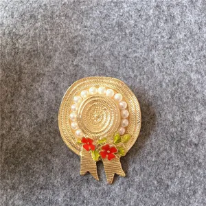 Détail d'une broche chapeau de paille dorée vintage avec fleurs rouges et perles.