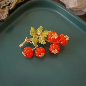 Dettaglio di una spilla barocca vintage con bacche di smalto rosso e foglie dorate.