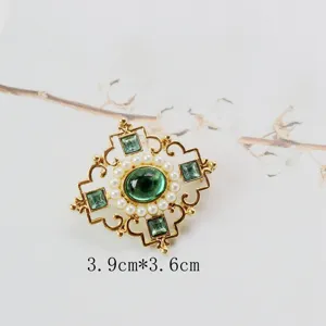 Detailed close-up view of a vintage gold brooch with green gemstones and pearls