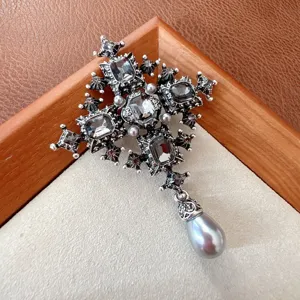 Close-up detail of a vintage silver cross brooch featuring grey crystals and pearl.