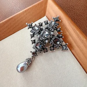 Detailed view of a vintage gothic black crystal cross brooch with a teardrop pearl