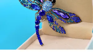 Close-up detail of a vintage blue rhinestone dragonfly brooch on a jewelry box.