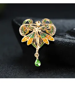 Vista detallada de un broche de ángel de oro de estilo barroco con cristales verdes.