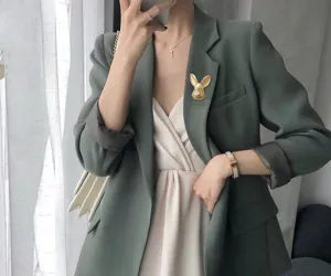 Gros plan d'une broche de lapin vintage en or mat sur le revers d'un blazer vert gris.