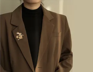 Gros plan d'une broche lapin en or mat vintage sur le revers d'un blazer marron.