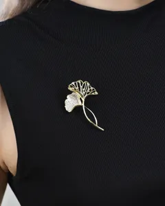 Gedetailleerd overzicht van een gouden ginkgoblad broche met sprankelende kristallen.