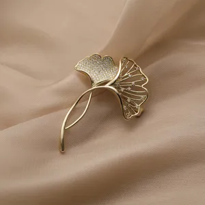 Close-up van elegante gouden ginkgobladbroche met sprankelende kristallen op zijde