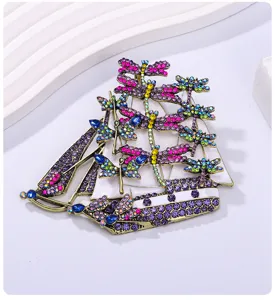 Intricate close-up of a vintage sailboat brooch adorned with colorful crystal dragonflies.