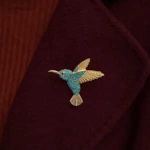 Macro view of an elegant gold hummingbird brooch featuring turquoise pave stones on wool