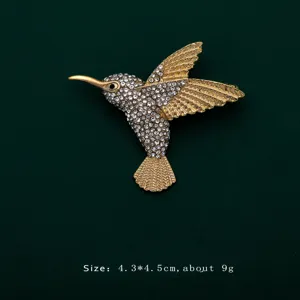 Detailed close-up of a sparkling rhinestone hummingbird brooch on green fabric