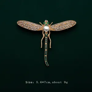 Detailed view of elegant gold dragonfly brooch featuring white pearl and green crystals