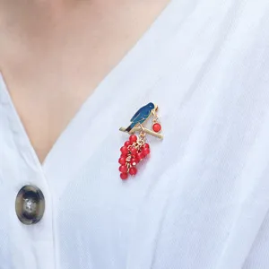 Elegant gold-tone bird brooch with red berry clusters worn on a white blouse detail