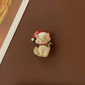 Close-up of a cute enamel cat brooch wearing a red Santa hat and holly for Christmas decor.