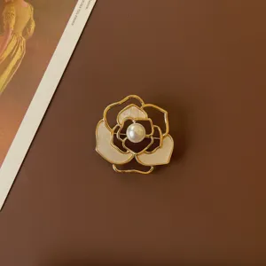 Macro detail of a vintage camellia brooch with white enamel petals and a central pearl