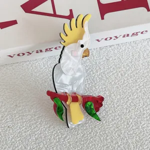 Detail shot of a white acrylic cockatoo brooch with yellow crest on a red branch.