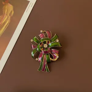 Close-up of a vintage baroque enamel brooch with green and magenta ribbon design.