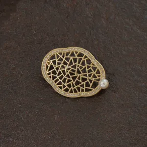 Detail shot of a vintage gold baroque brooch with geometric patterns and pearl accent.