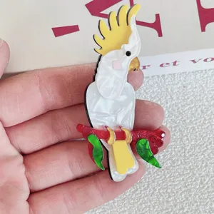 Detailed view of a white acrylic cockatoo brooch on a red branch with green leaves.