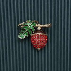 Exquisite close-up of vintage baroque acorn brooch featuring red rhinestones and green leaf.