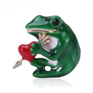Detail of a green frog brooch holding a red heart with a gold arrow and rhinestones.