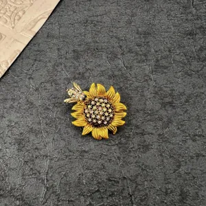 Macro detail of vintage sunflower brooch with crystal bee on textured grey background.