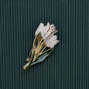 Detail view of a vintage baroque white tulip brooch with green leaves and gold plating