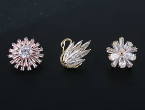 Primer plano de elegantes broches de circón en forma de cisne y flores con baño de oro rosa.